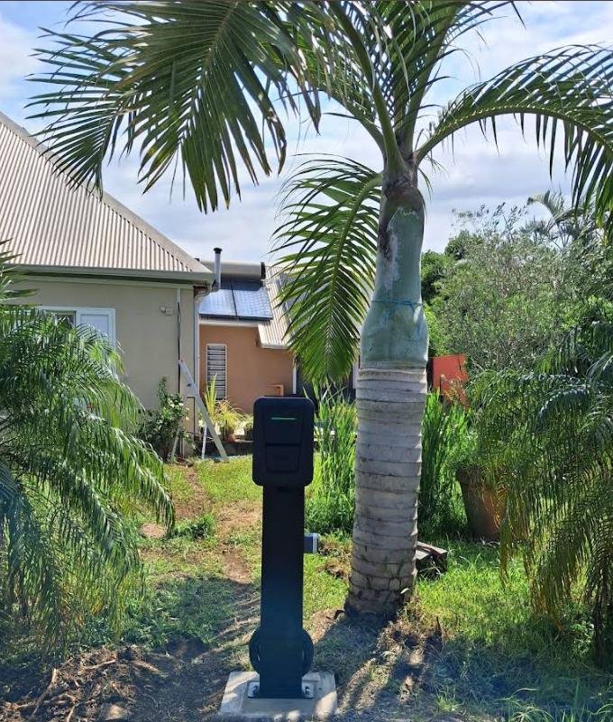 Borne de recharge pour véhicule électrique installée sur pied et massif béton dans un jardin.
